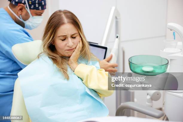 young woman feeling pain, holding her cheek with hand at dentist's office.toothache concept. - emergencies and disasters 個照片及圖片檔