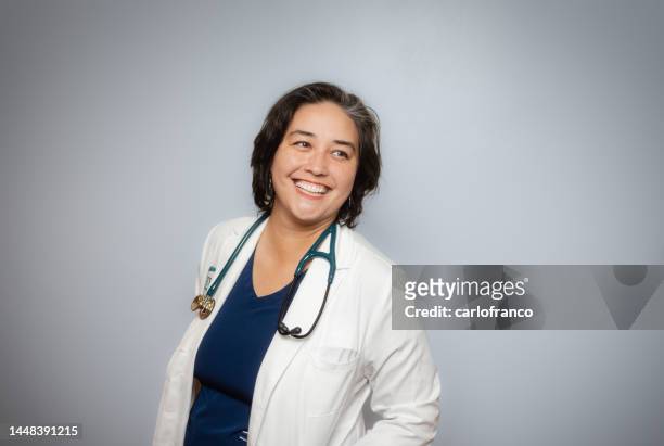 studio portrait - female doctor - soft grey background - positive emotion - white coat- looking to the side - female doctor portrait stockfoto's en -beelden
