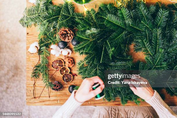 a woman is making a christmas wreath with pinaceae branches on a wooden table with fairy lights - legno di pino foto e immagini stock