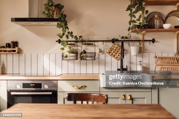 empty kitchen island with marble surface in foreground, green vintage countertop with drawers and pendant lights hanging above, lots of flowers in jars, blurred background - keuken stockfoto's en -beelden