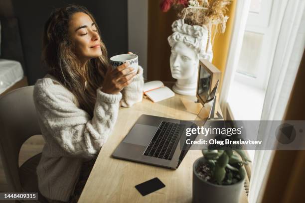 young pretty woman enjoying morning coffee and working on laptop at home. freelance business, distant job - lanterne photos et images de collection