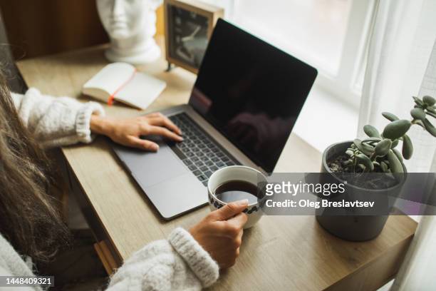 woman's hand holding cup of black coffee. wasting time in social media on laptop. morning news - clock person desk stockfoto's en -beelden
