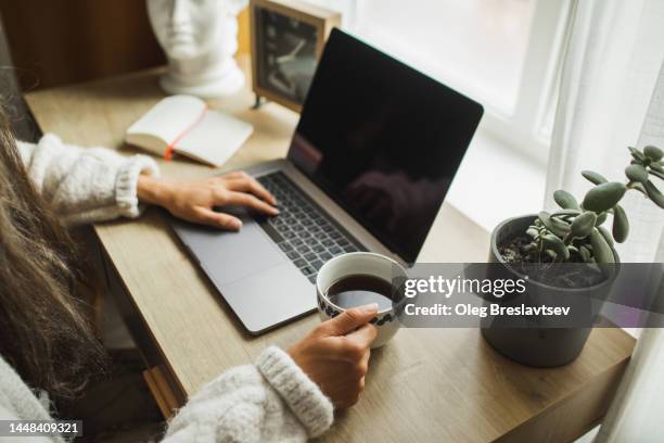 woman's hand holding cup of black coffee. wasting time in social media on laptop. morning news - clock person desk stock pictures, royalty-free photos & images