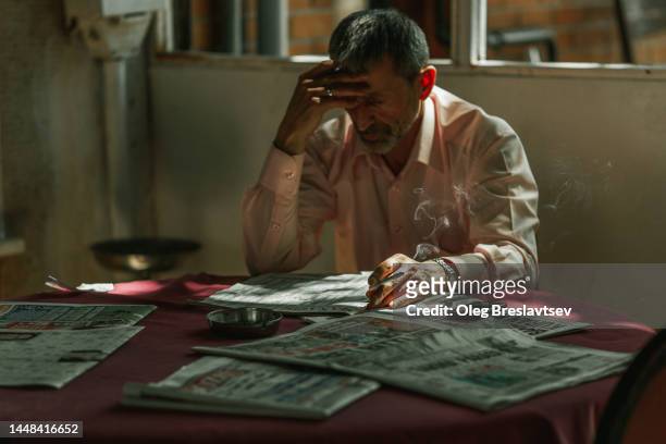 thoughtful sad senior man smoking and reading newspapers in dark room - turkey middle east stock pictures, royalty-free photos & images