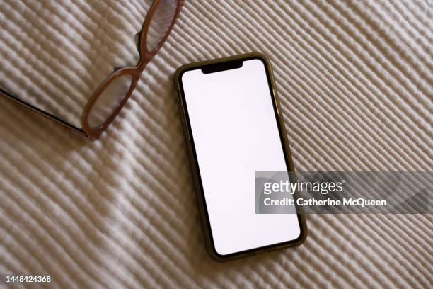 smart phone with blank screen on white bedspread with eyeglasses in view - phone still life stock pictures, royalty-free photos & images
