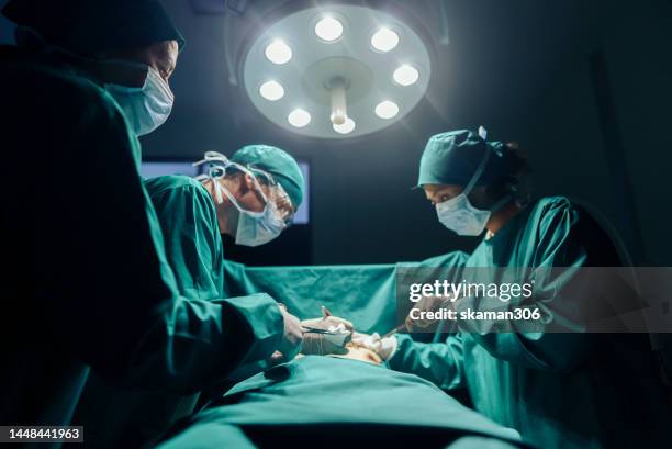 teamwork and cooperation three surgeons performing operating on a patient in the hospital's operating room - operatiekamer stockfoto's en -beelden