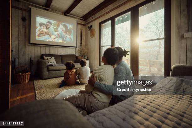 back view of relaxed black family watching a movie at home. - projectieapparatuur stockfoto's en -beelden