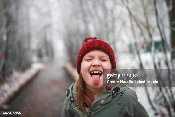 happy child enjoys first snow. child in hat and jacket is squinted and catches snowflakes with his tongue. close up and copy space. - human tongue stock pictures, royalty-free photos & images