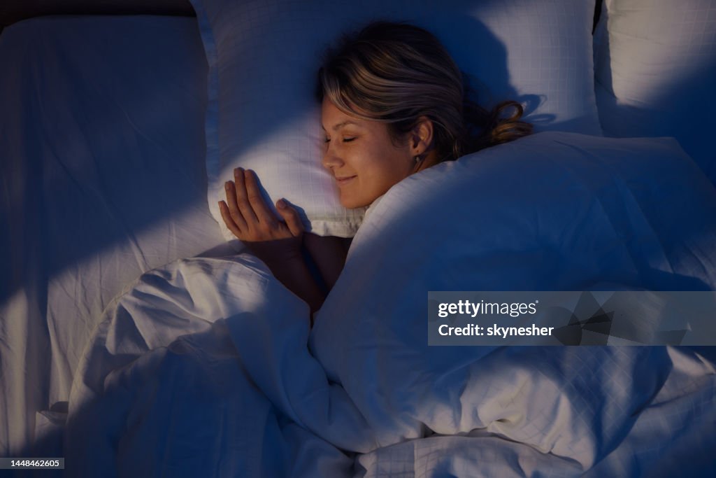 Vista acima da mulher sorridente dormindo na cama.
