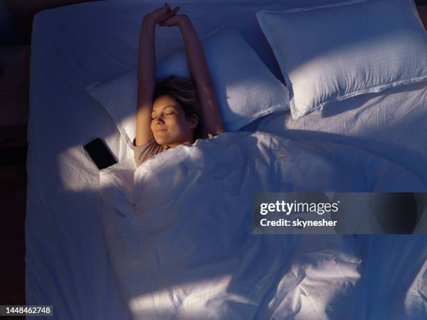 above view of serene woman stretching in bed. - pyjamas stock pictures, royalty-free photos & images