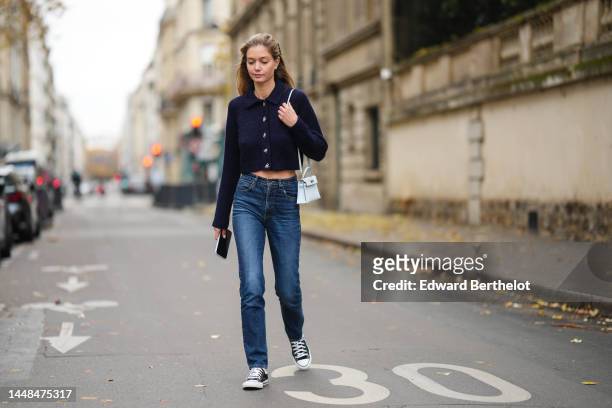 Mathilde Frachon wears a black ribbon knot in the hair, a navy blue wool / crystals buttons / cropped pullover, a blue white shiny leather mini Kelly...