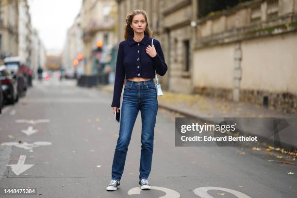 Mathilde Frachon wears a black ribbon knot in the hair, a navy blue wool / crystals buttons / cropped pullover, a blue white shiny leather mini Kelly...