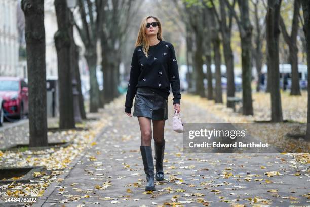 Mathilde Frachon wears black sunglasses, gold earrings, a black with embroidered white and pale pink bees pattern pullover, a black shiny leather...