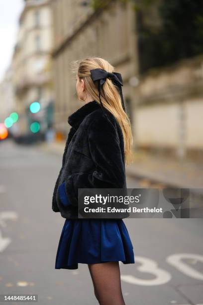 Mathilde Frachon wears gold earrings, a black fur coat, a navy blue velvet silk short dress, black transparent tights, during a street style fashion...