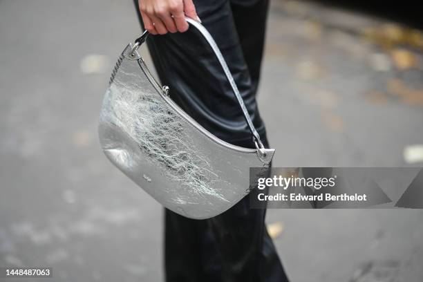 Natalia Verza wears a silver shiny varnished leather shoulder bag, black shiny leather large wide legs pants, during a street style fashion photo...