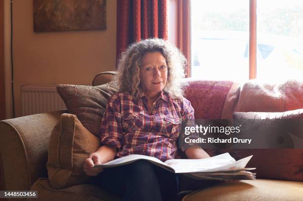 portrait of a mature woman sitting on the sofa reading a newspaper - living room stock pictures, royalty-free photos & images