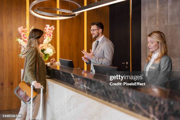 addetto alla reception dell'hotel maschile che assiste l'ospite femminile - offrire un servizio foto e immagini stock