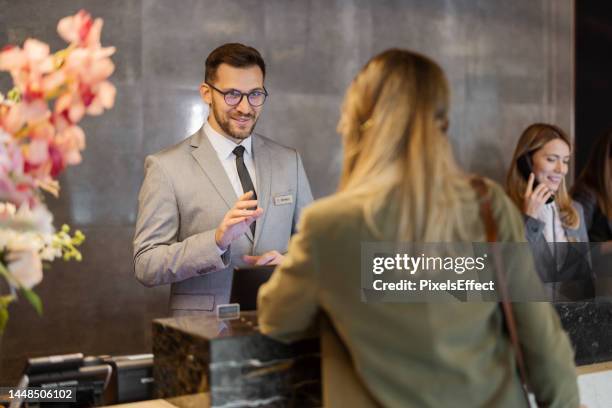 male receptionist at front office talking with female guest - hotel occupation stock pictures, royalty-free photos & images