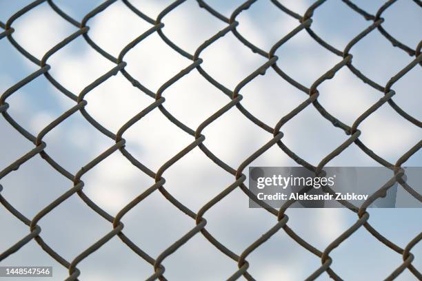 metal wire mesh on a background of blue sky with white clouds. fence, barbed wire. the concept of restriction of freedom. sanctions against the country. problems, economic and financial crisis due to military actions and offenses. - prison fence stock pictures, royalty-free photos & images