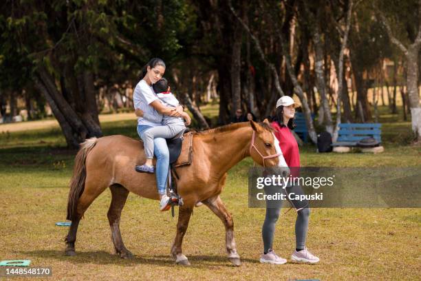 fürsorgliche frau, die einen kleinen jungen hält, während sie reiten - enable horse stock-fotos und bilder