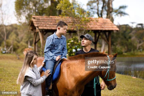 junger mann und frau nehmen einen jungen mit down-syndrom auf einen ausritt auf dem bauernhof - horse and male and riding stock-fotos und bilder