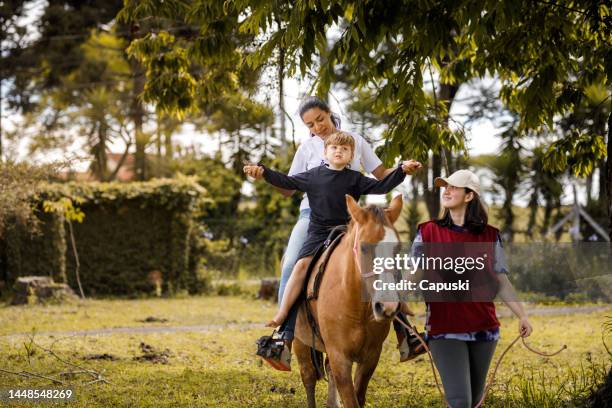 little boy riding a horse with therapists support - special education stock pictures, royalty-free photos & images
