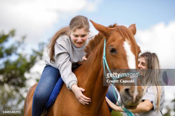 mädchen lernt, wie man den hals eines pferdes streichelt, während es während der pferdegestützten therapie auf dem rücken sitzt - enable horse stock-fotos und bilder