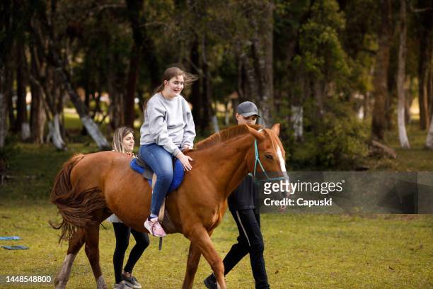 mädchen mit zerebralparese macht therapie mit pferden mit hilfe von betreuern - horse and male and riding stock-fotos und bilder