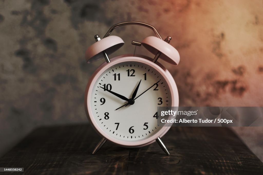 Pink alarm clock wooden desk against weathered wall