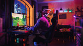 Hyped Gamer Playing PvP Shooter Video Game in Which Players Fight in a Battle Royale Tournament on His Personal Computer. Room and PC with Neon Lights. Stylish Black Man in Cozy Room at Home.