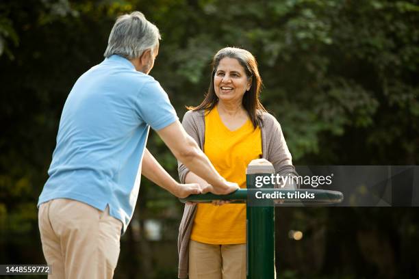 senior couple spinning exercise equipment at playground - indian elderly couple stock pictures, royalty-free photos & images