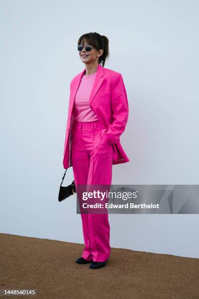 Sophie Marceau wears earrings, sunglasses, a pastel pink t-shirt, a neon pink oversize blazer jacket, matching suit pants, a Jacquemus bag, black...