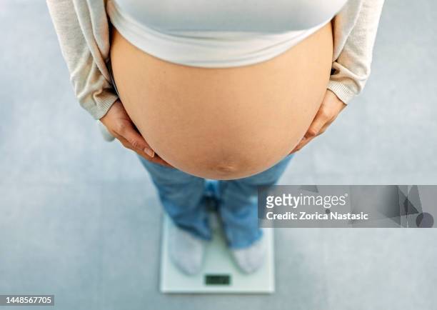 jeune femme enceinte debout sur une balance de poids - kilogram photos et images de collection