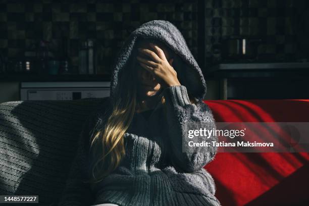 a young woman in a hoodie is sitting on a red sofa at home. the concept of depression and mental disorders. - unrecognisable person stock pictures, royalty-free photos & images