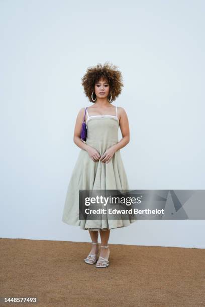 Lena Mahfouf aka Lena Situations wears large earrings, an off-shoulder beige pleated midi dress, a purple Jacquemus bag, high heeled shoes, outside...