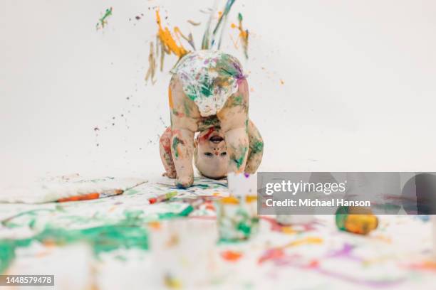 a young toddler, covered in paint, plays with washable paint on a white backdrop. - baby paint stock-fotos und bilder