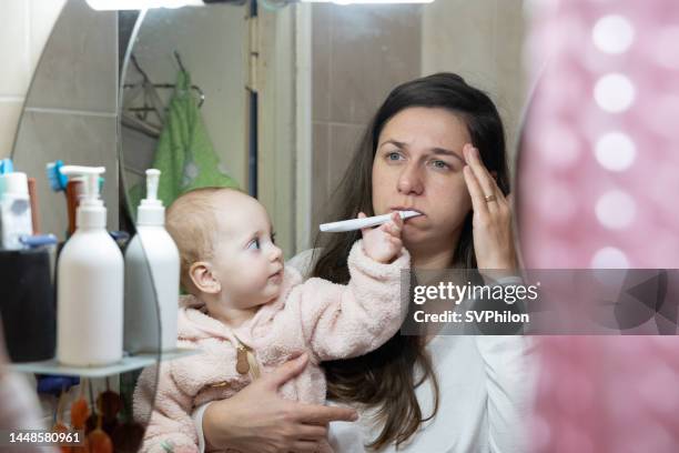 the mother holds the child in her arms and brushes her teeth with pain in her head. - tired mother stock pictures, royalty-free photos & images