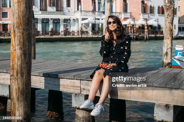 woman sitting on dock and eating strawberry in venice - venice italy bildbanksfoton och bilder