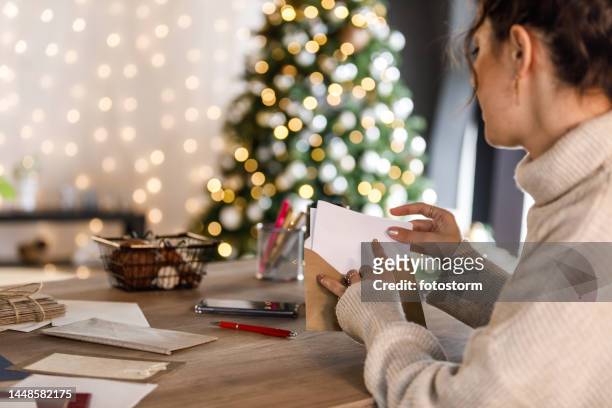 mujer joven poniendo la carta de navidad que escribió en un sobre - escribir a mano fotografías e imágenes de stock