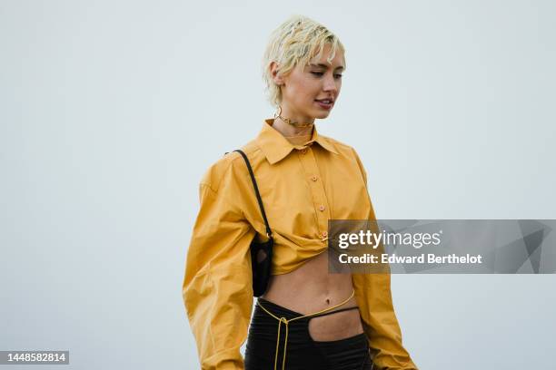 Iris Law wears an orange oversized cropped shirt, a slit skirt, a black bag outside the "Le Raphia" Jacquemus show on December 12, 2022 in Le...