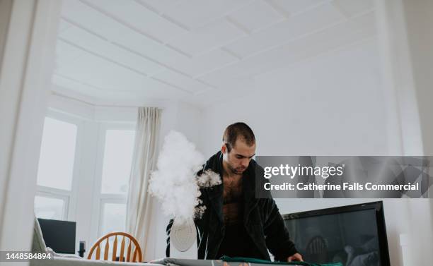 a man wearing a dressing gown irons a green t-shirt - interim stock pictures, royalty-free photos & images