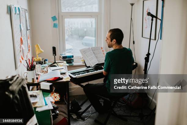 a man in a small creative space plays a keyboard and sings - songwriter stock-fotos und bilder