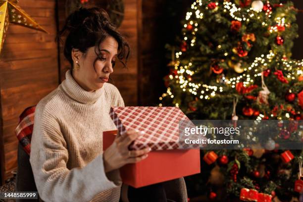 junge frau sitzt am weihnachtsbaum und öffnet eine geschenkbox - disappointment stock-fotos und bilder