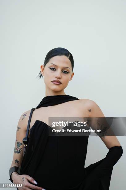 Gabbriette wears a black long off shoulder and low neck dress with integrated corset, outside the "Le Raphia" Jacquemus show on December 12, 2022 in...