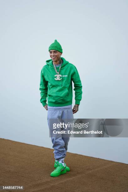 Central Cee wears a neon green wool ribbed beanie hat from Marni, a Chanel large logo necklace, a green hoodie sweater from Jacquemus, gray jogger...