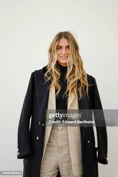 Joana Preiss wears a black long coat, a beige oversized blazer jacket, a black turtleneck pullover, beige flared pants, outside the "Le Raphia"...