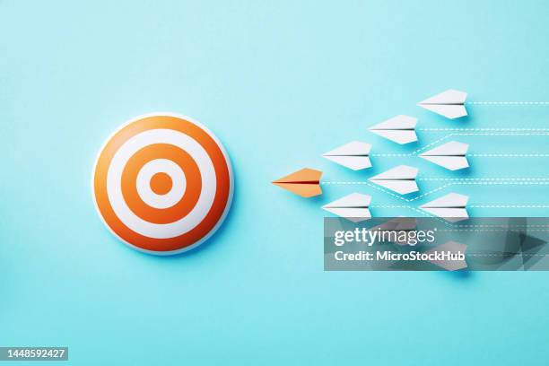 paper planes moving towards an orange bull's eye target on blue background - aiming stock pictures, royalty-free photos & images