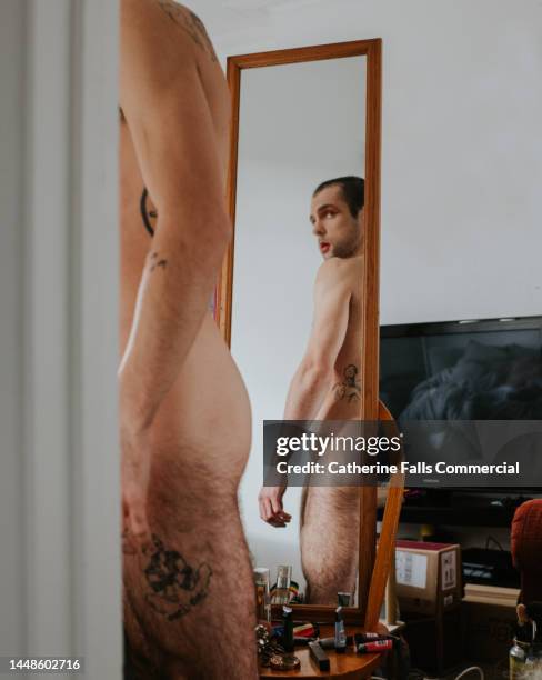 a tattooed naked man looks at himself in a full length mirror - self destruction stock pictures, royalty-free photos & images