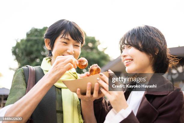 japanese mother and daughter eating takoyaki outdoors. - takoyaki stock pictures, royalty-free photos & images