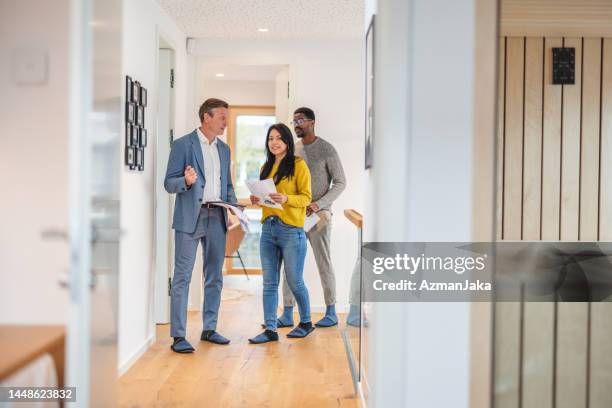 adult caucasian male real estate agent selling and showing the modern apartment to his diverse young clients that are standing next to him in the fancy apartment - business couple showing stockfoto's en -beelden